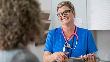 A nurse wearing blue scrubs and a pink stethoscope, practicing ethics in nursing while talking to a patient