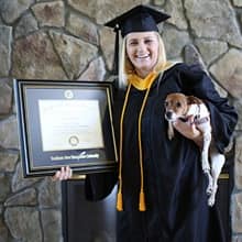 Kimberly Cartier in a cap and gown, holding her diploma in one hand and her dog in another