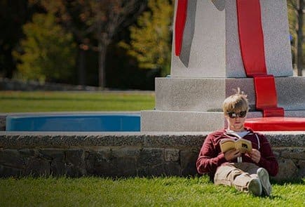 Person reading a book by a monument.