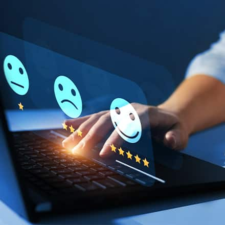 A customer experience professional typing on a laptop with three emoji icons representing levels of satisfaction