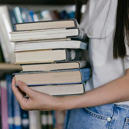  A student holding a stack of books in a library working on academic referencing for their research paper.