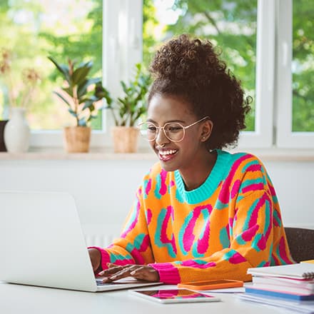 An undergraduate student wearing a bright orange shirt, completing her accelerated master's program coursework on a laptop