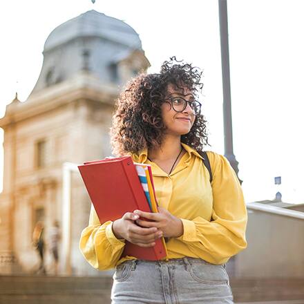 A person in a yellow shirt holding binders and considering affordable online colleges.