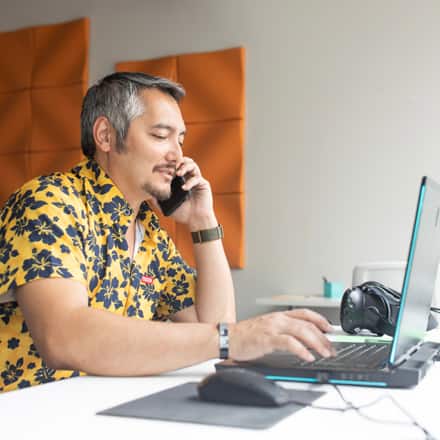 A student working on his Bachelor of Arts degree on his laptop while on a phone call with his advisor.