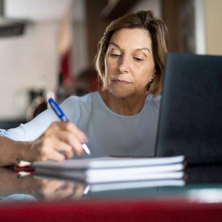 A person researching how to go back to college on a laptop and taking notes with a pen