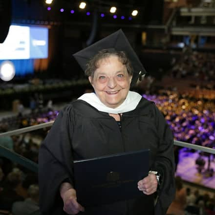 Mary Beth Dayley '24G, an SNHU Masters in English and Creative Writing graduate, in a cap and gown holding her diploma.