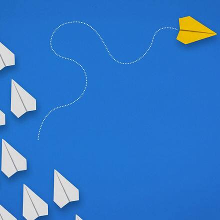 White paper planes and one yellow plane going in a different direction on a blue background 