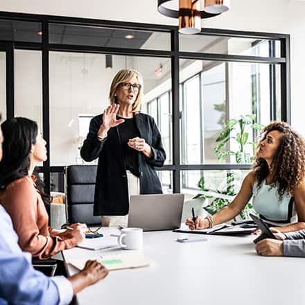 A director of operations standing at the end of a table running a team meeting