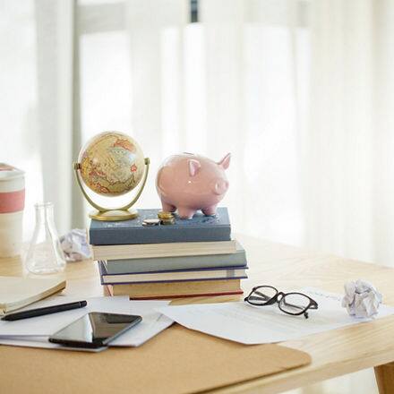 A desk with papers, a phone, and a stack of books with a piggy bank and globe on top.