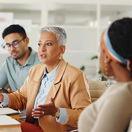 Three colleagues sitting at a meeting table, practicing conflict resolution skills.