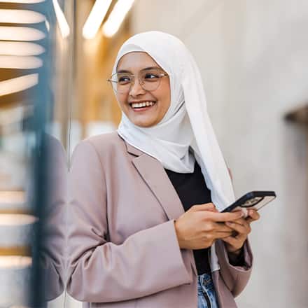 A woman wearing a suit jacket and hijab holding her phone.