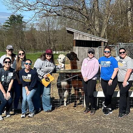 A group of 8 volunteers and 2 alpacas at the Joppa Hill Farm Spring Maintenance service project during Global Days of Service