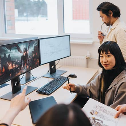 A group of game developers sitting around a desktop working on a video game design.