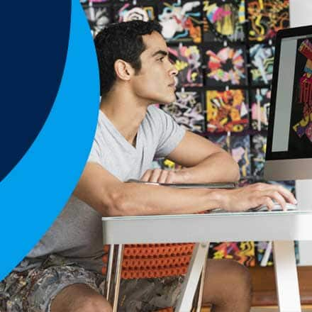 A graphic designer working at his desk next to a blue background.