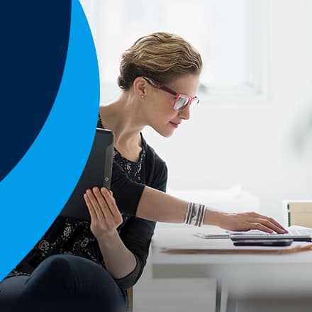 A woman who earned an online MBA holding a tablet and working on a laptop.