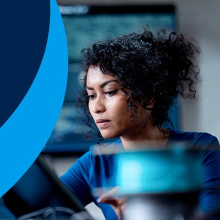 A woman working in information technology sitting at a desk with an outline of a hand holding a phone to the left on a blue background