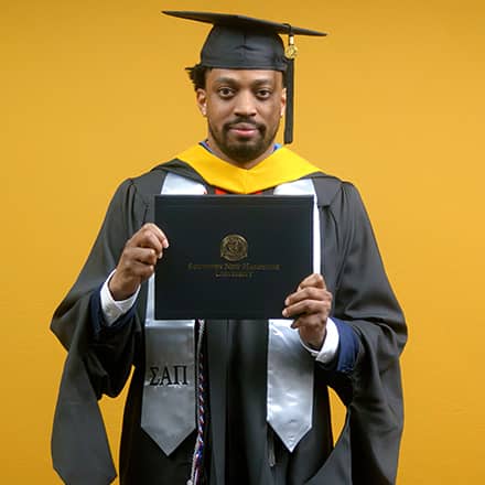 Josiah Lee, a 2025 master's in cybersecurity graduate from SNHU, wearing a cap and gown and holding his diploma.