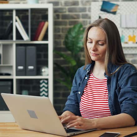 A woman sitting at a table typing on a laptop in an office setting.