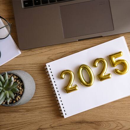 2025 represented in gold lettering on a notebook with a pen, plant and laptop beside it