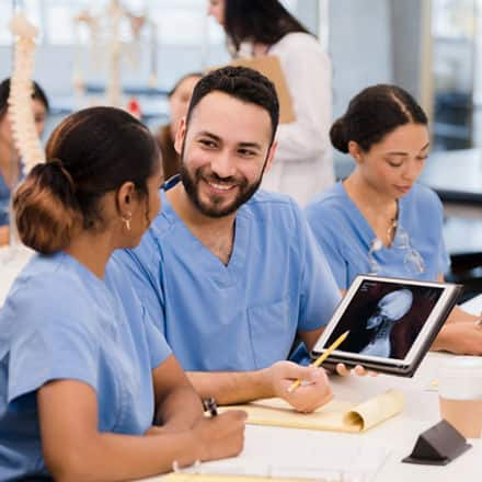 Three nurses in blue scrubs, working together in a professional development seminar