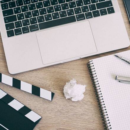 A screenwriters desk with a laptop, movie clapper, headphones a script and crumpled up paper of screenplay drafts. 