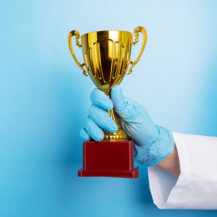 A nurse with a blue glove on holding an award in front of a blue background.