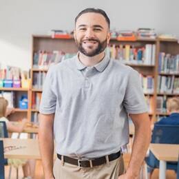 Stephen Goulakos, a 2022 graduate from SNHU with a BA in Psychology and a concentration in Mental Health, standing in a classroom with kids working at their desks.