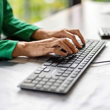 A person wearing a green top typing on a keyboard working as a technical writer.