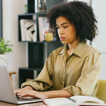 A student sitting at her laptop working on her college thesis paper.