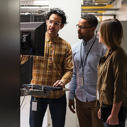 Three IT professionals working at a computer terminal.