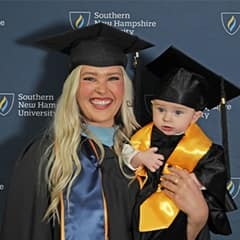 Casey Rasmussen '23, an SNHU MEd graduate, holding her son, Rockwell, who's also wearing a cap and gown