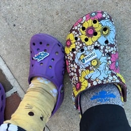 A purple clog next two a floral clog, both with SNHU logo charms