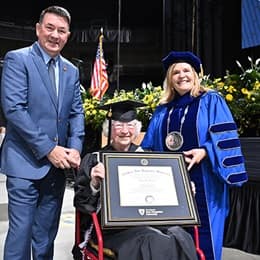 Annette Roberge holding her SNHU diploma between her son, left, and SNHU President Lisa Marsh Ryerson, right