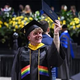 A graduate in a cap and gown, holding up a diploma during SNHU's Commencement Weekend