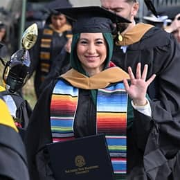 A graduate in a cap and gown, holding up a diploma after SNHU's Commencement Weekend