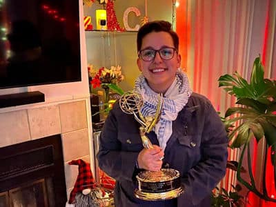 Elanna Rubenstein, who earned a master's in communication from SNHU, standing in a living room holding a trophy.