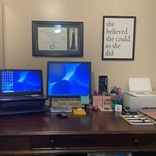 A laptop connected to a desktop on a desk with a laptop. An SNHU diploma and motivational sign hang on the wall.
