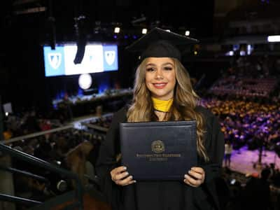 Tiare Hazen, an SNHU graduate, wearing her cap and gown and holding her diploma.