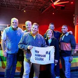 Six members of New Hampshire College's Class of ’89 at a roller-skating rink, holding a sign with the text New Hampshire College #1