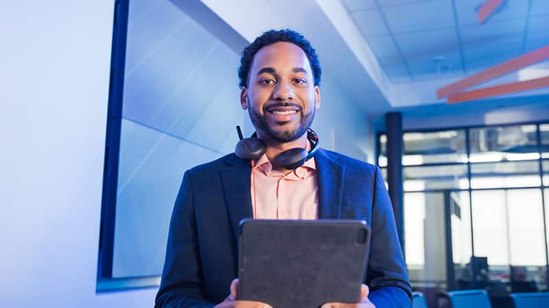 2022 online degree graduate Gary Walker, standing in front of a laptop with a pair of headphones resting on his shoulders.