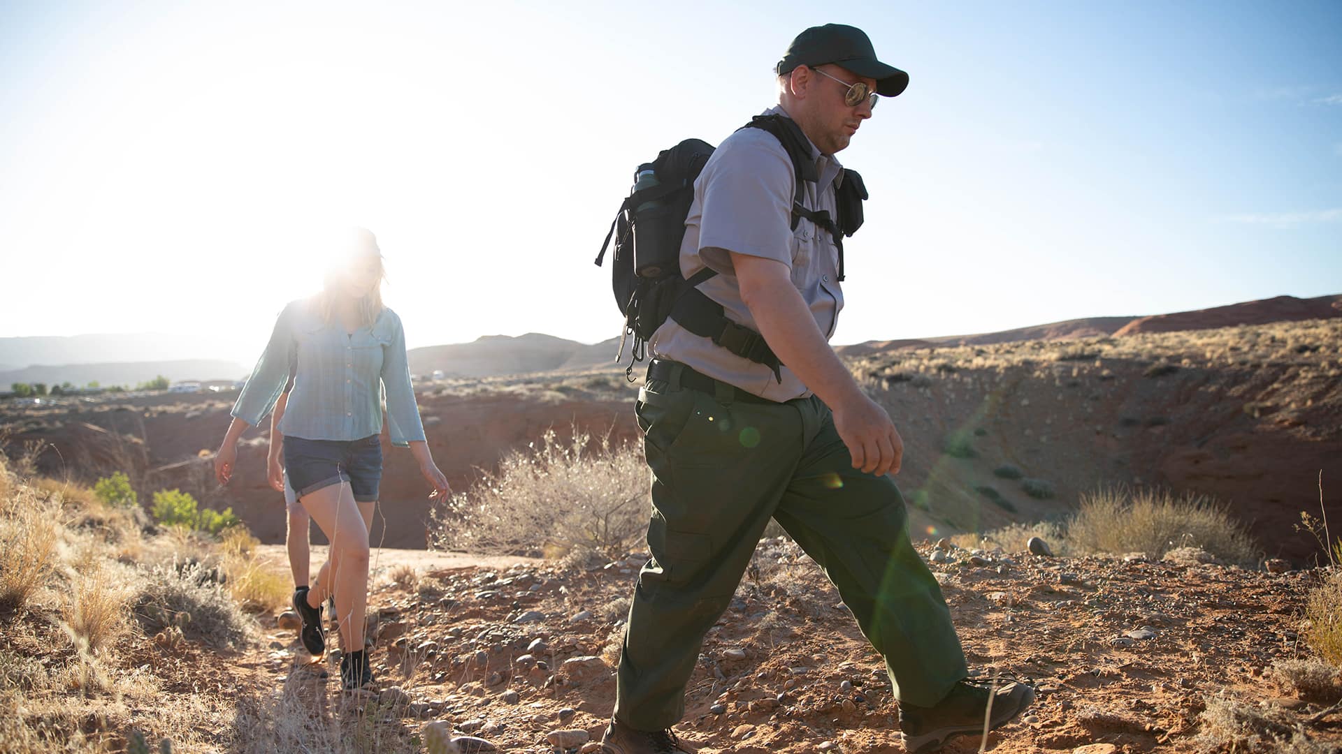 John Roos, who earned his SNHU degree in 2018, wearing a park ranger uniform, baseball cap and sunglasses as he leads two people on a hike through desert terrain. 