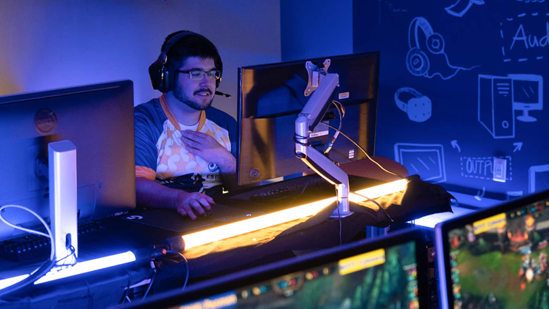 Sultan Ahktar, who earned his degree from SNHU in 2019, wearing his esports uniform and headset with  microphone playing a video game on a desktop computer.