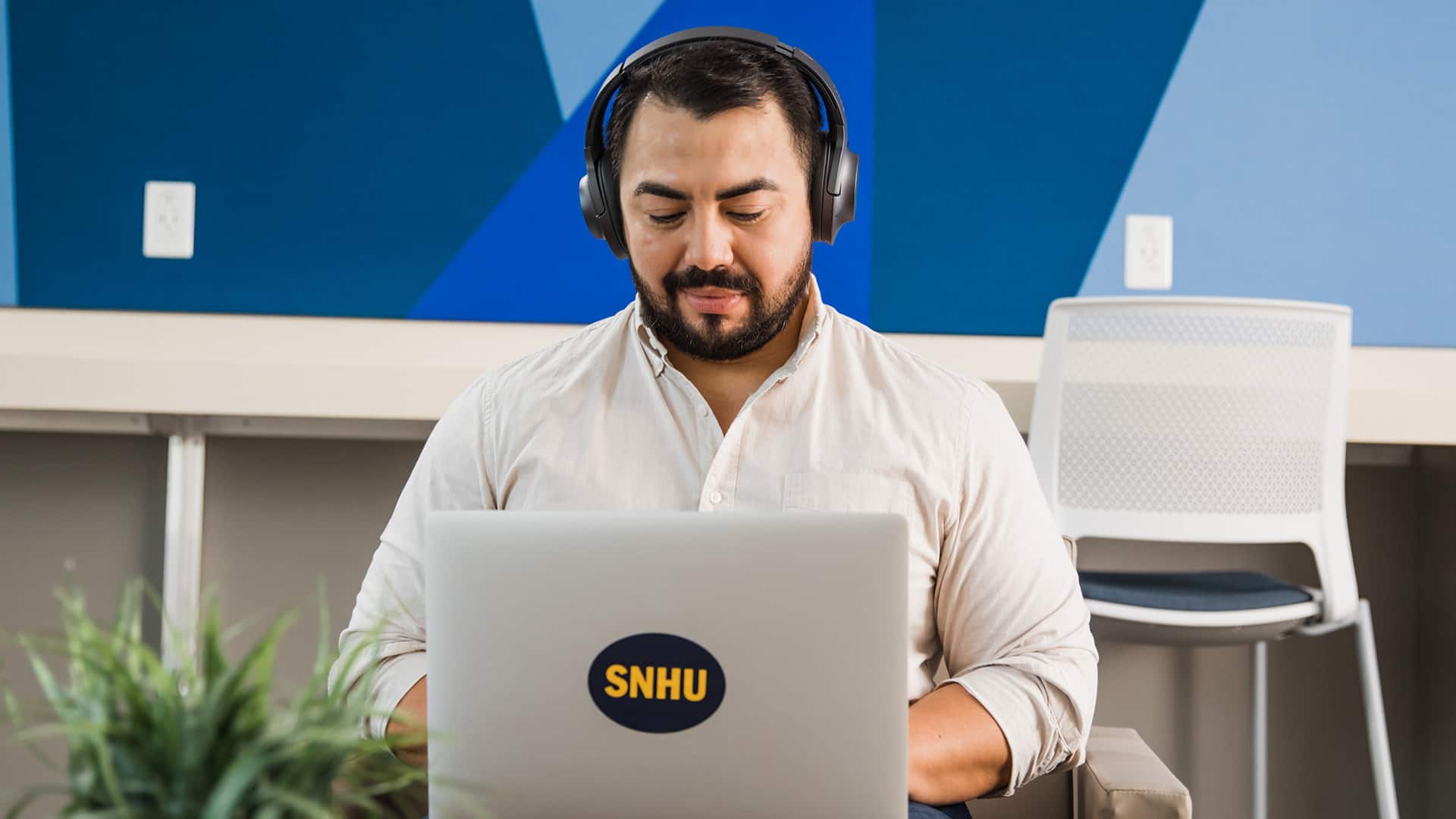 2021 Bachelor's in Graphic Design and Media Arts alum Jesus Suarez, wearing headphones while working from a laptop computer.