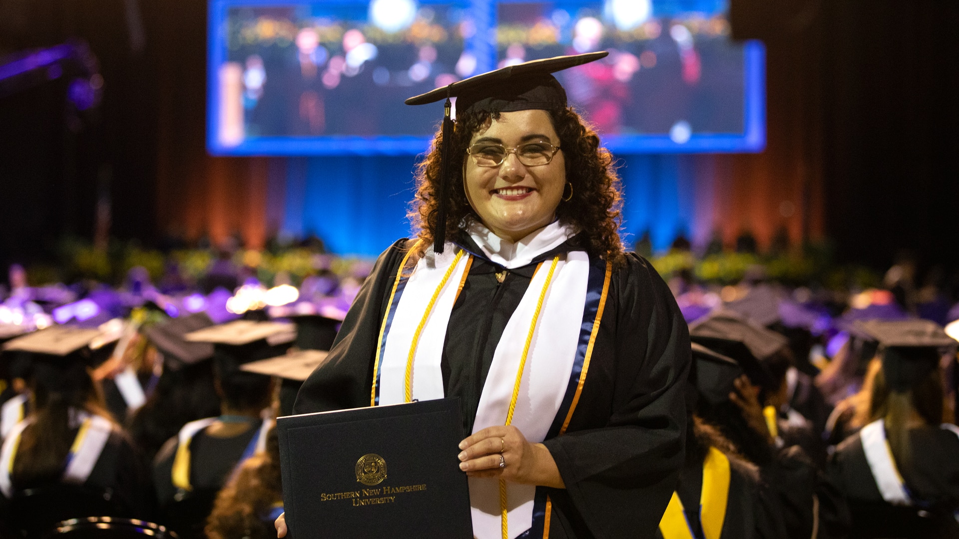 Sarah Childress, in cap and gown, smiling at a recent commencement ceremony at the SNHU arena.