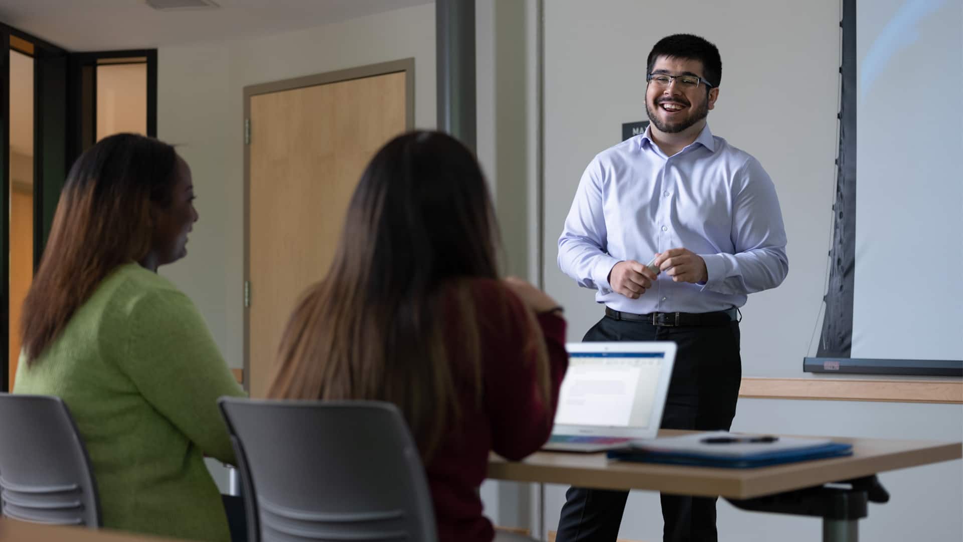 Sultan Ahktar, who earned his degree from SNHU in 2019, standing in front of two women in a classroom.