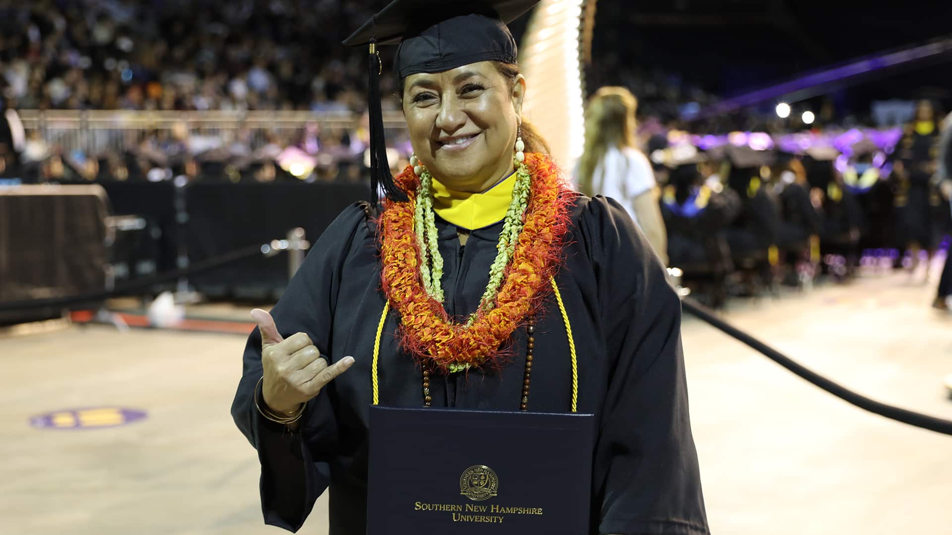 Sharla Kaleihua Kahale-Miner, holding her diploma and making a traditional Hawaiian hand gesture, at the 2023 Southern New Hampshire University commencement ceremony.