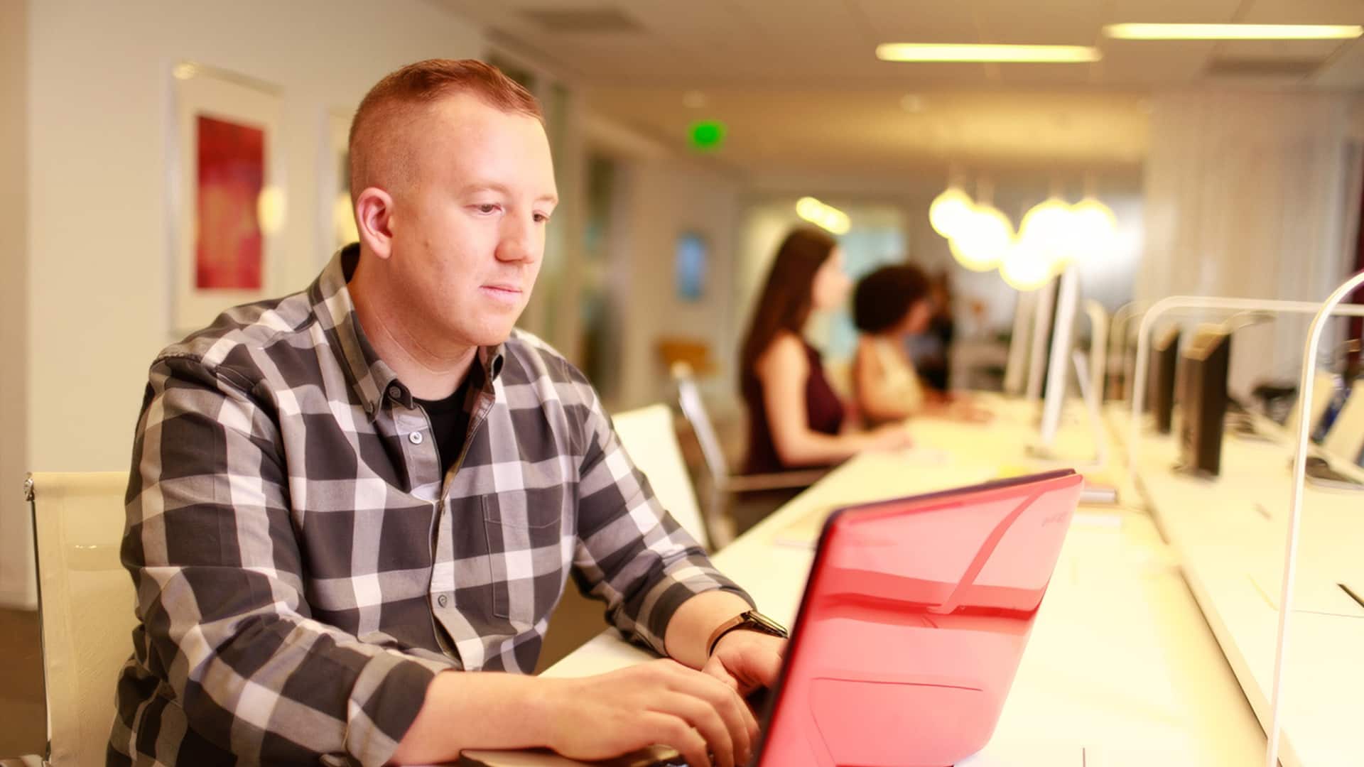 Kevin Deveraux wearing a black and grey plain buttondown shirt working on a red laptop.