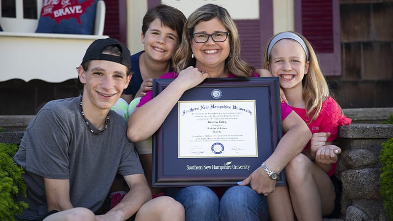 Kristina Libby, sitting on outside steps with her three children surrounding her while she holds her 2017 online nursing degree.