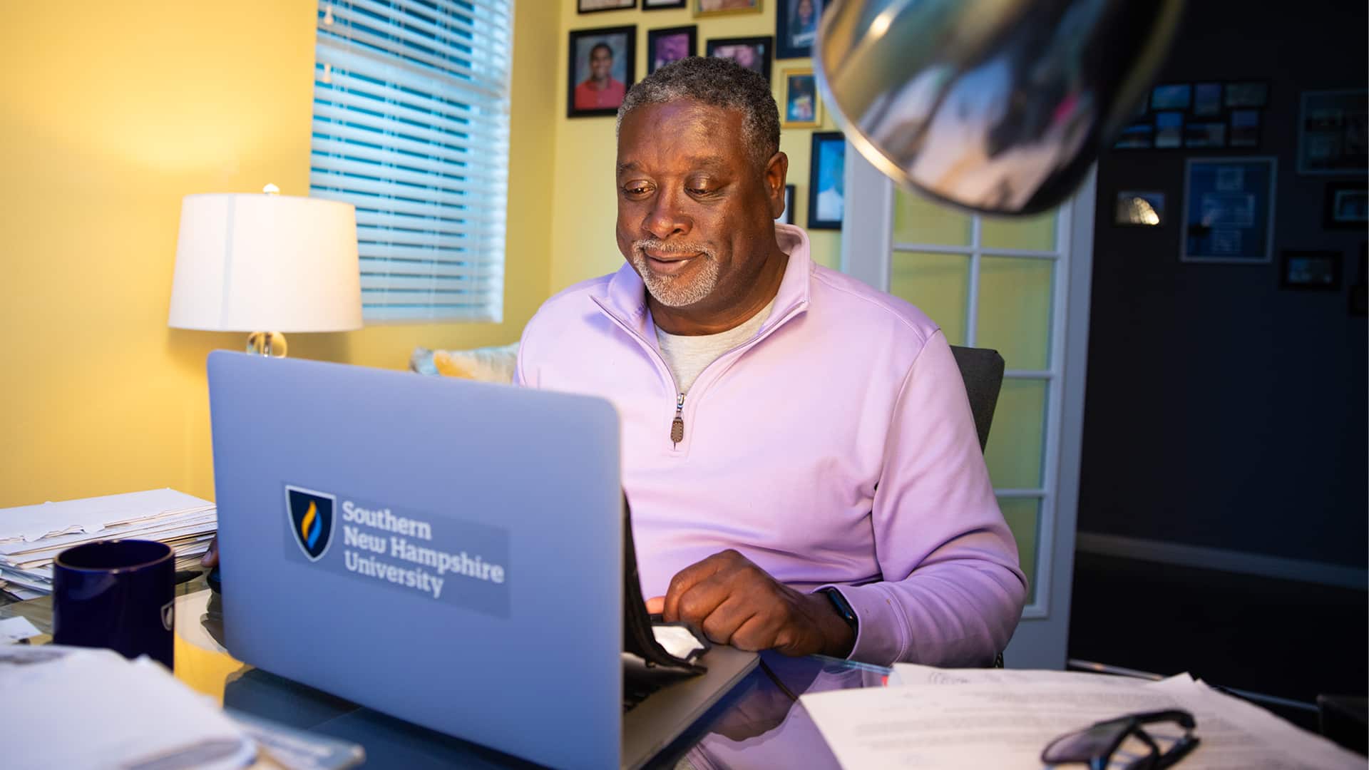 Corey Dantzler, who earned a graduate certificate in athletic administration in 2023, in his home office working on a laptop that has an SNHU sticker on the front of it.