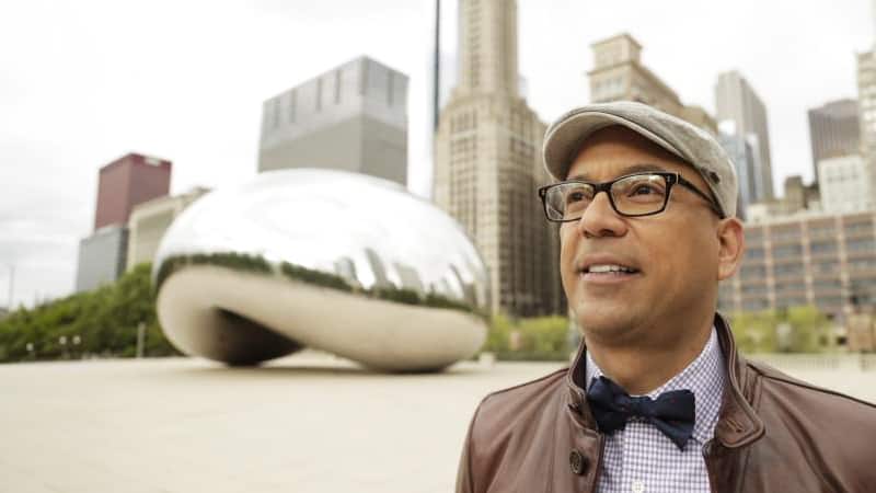 Jose Medina wearing a bow tie and button down shirt with a large metal sculpture in the background.